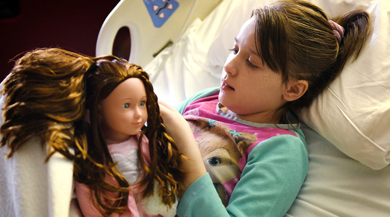 Lacey plays with her doll in a Riley hospital bed