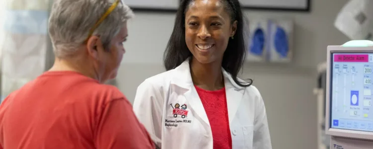 Riley provider smiles while talking with a patient in a clinic exam room.